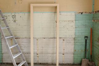 Mur intérieur en partie dégarni pendant un chantier de rénovation, échelle et outils au pied